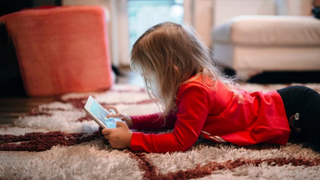 Child sitting on the floor, holding and watching connected tablet